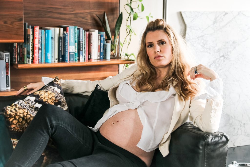 Nina lays back on a couch, pregnant belly exposed and looking glamorous as fuck