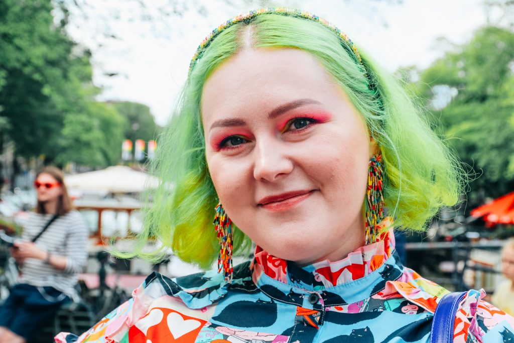 beautiful girl with pale skin and bright green hair, bright pink eyeshadow smiling into the cmera